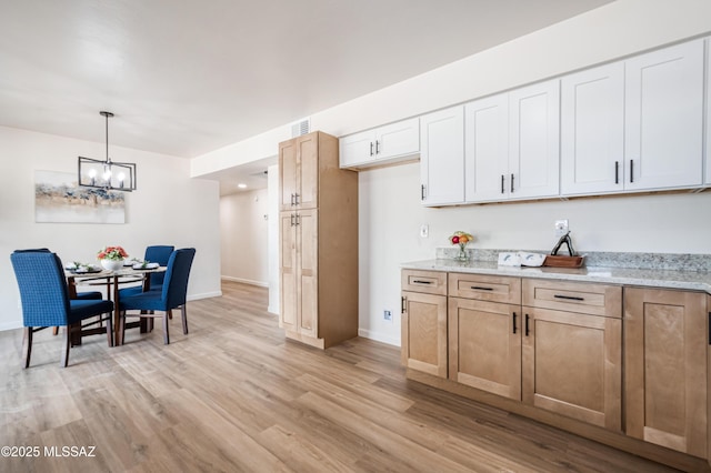 kitchen with light wood finished floors, a notable chandelier, light stone counters, and decorative light fixtures