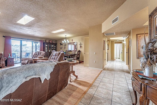 living area featuring an inviting chandelier, a skylight, visible vents, and a wood stove