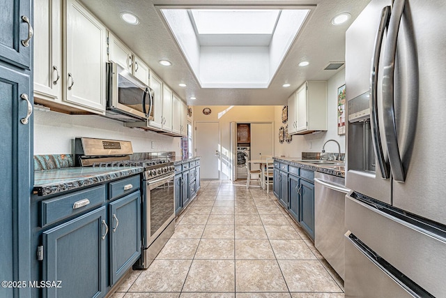 kitchen featuring blue cabinetry, washer / dryer, appliances with stainless steel finishes, a raised ceiling, and a sink