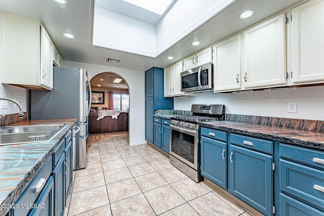 kitchen featuring visible vents, blue cabinetry, appliances with stainless steel finishes, arched walkways, and a sink