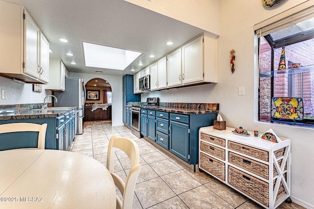 kitchen featuring dark countertops, blue cabinets, arched walkways, and stainless steel appliances