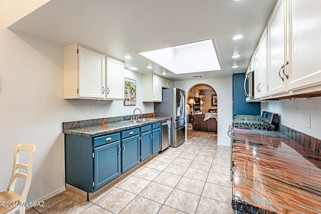 kitchen featuring a skylight, a sink, white cabinetry, dark countertops, and blue cabinets