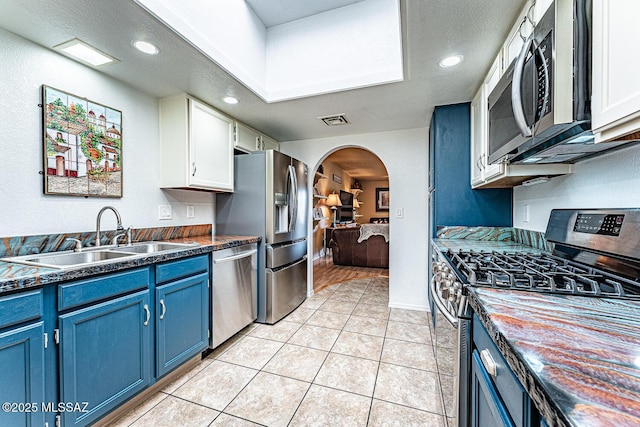 kitchen featuring dark countertops, blue cabinetry, arched walkways, stainless steel appliances, and a sink