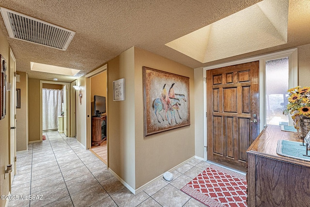 foyer with visible vents, a textured ceiling, a skylight, light tile patterned flooring, and baseboards