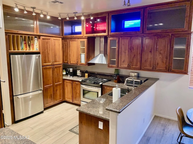 kitchen featuring gas stove, a peninsula, freestanding refrigerator, a sink, and wall chimney range hood