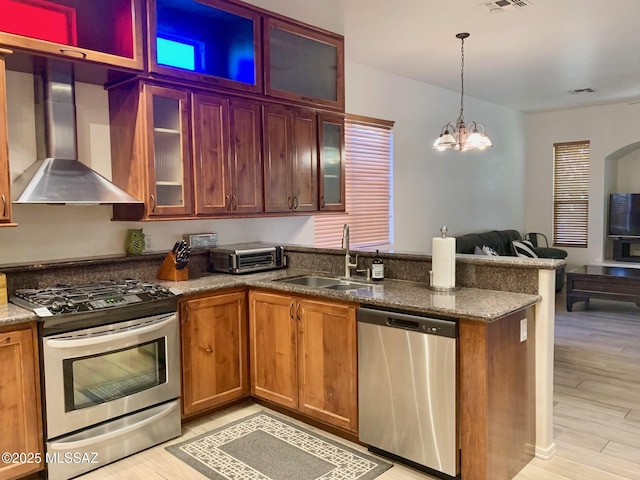 kitchen with a peninsula, a sink, stainless steel appliances, wall chimney range hood, and open floor plan