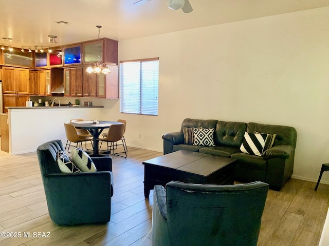 living area featuring visible vents, light wood-style flooring, ceiling fan with notable chandelier, and baseboards