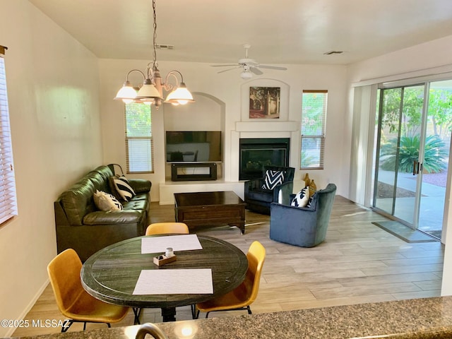 living area featuring a glass covered fireplace, ceiling fan with notable chandelier, visible vents, and light wood finished floors