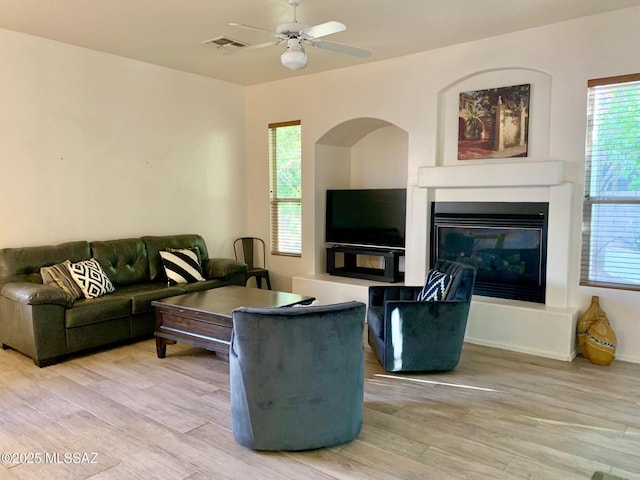 living area featuring a glass covered fireplace, visible vents, wood finished floors, and a ceiling fan