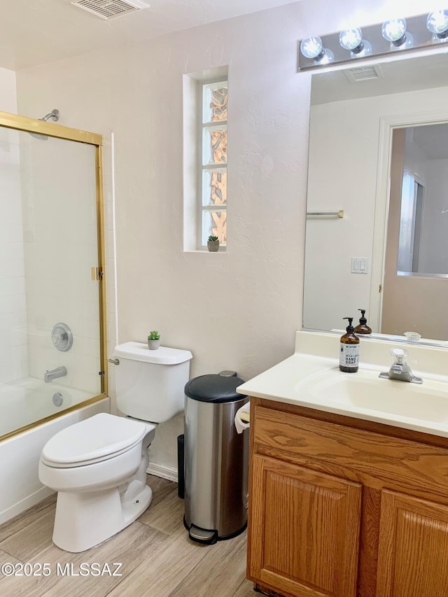 full bath with vanity, wood finished floors, visible vents, toilet, and combined bath / shower with glass door