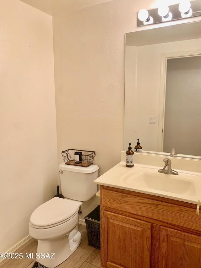 bathroom with toilet, vanity, baseboards, and wood finished floors