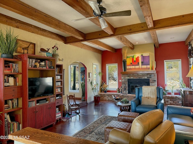 living room featuring beam ceiling, plenty of natural light, a fireplace, and ceiling fan