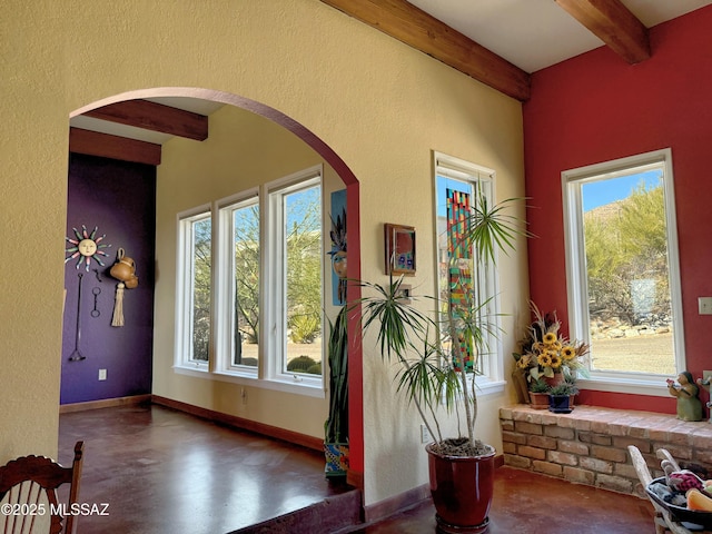 foyer featuring baseboards, arched walkways, concrete flooring, beamed ceiling, and a textured wall