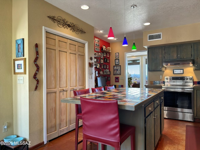 kitchen with visible vents, under cabinet range hood, stainless steel electric stove, a textured ceiling, and tile counters