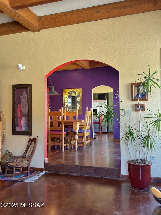 dining space featuring arched walkways, beam ceiling, concrete floors, and a textured wall