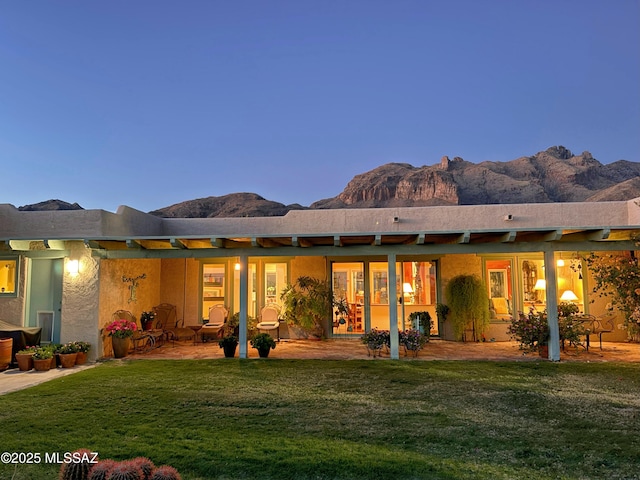 rear view of house with a yard, stucco siding, a mountain view, and a patio area