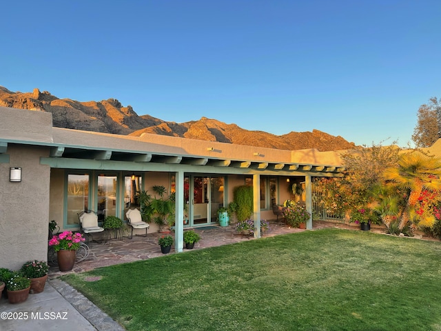 back of house with a patio area, a lawn, a mountain view, and stucco siding