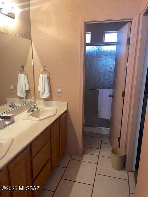 bathroom featuring tile patterned flooring, double vanity, a stall shower, and a sink