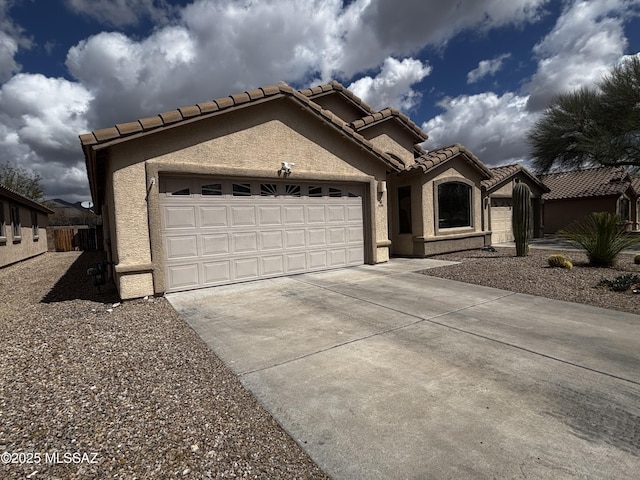 mediterranean / spanish house with stucco siding, a garage, driveway, and a tiled roof