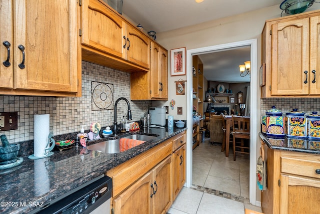 kitchen with a sink, dark stone counters, stainless steel dishwasher, and light tile patterned floors