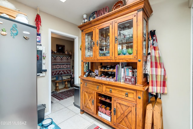 kitchen featuring light tile patterned flooring, brown cabinets, glass insert cabinets, and freestanding refrigerator