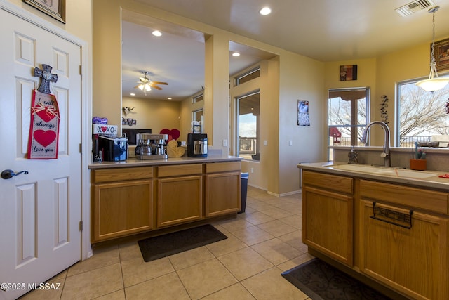 kitchen featuring visible vents, ceiling fan, light tile patterned floors, brown cabinetry, and a sink