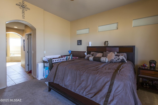 carpeted bedroom with arched walkways and tile patterned floors