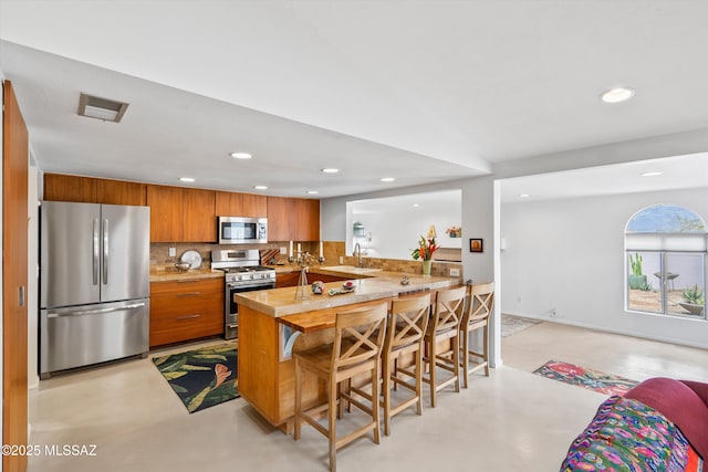kitchen featuring concrete floors, visible vents, appliances with stainless steel finishes, and brown cabinetry