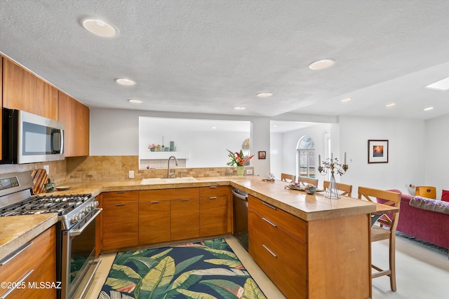 kitchen with a sink, a kitchen breakfast bar, backsplash, appliances with stainless steel finishes, and a peninsula