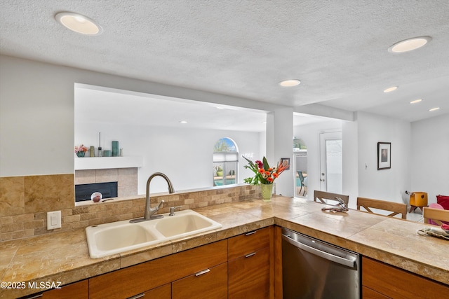 kitchen featuring tasteful backsplash, dishwasher, a fireplace, brown cabinetry, and a sink