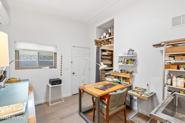 office area featuring light wood finished floors, baseboards, visible vents, and a wall mounted air conditioner