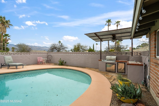 view of swimming pool featuring an outdoor kitchen, a patio, a fenced backyard, and ceiling fan