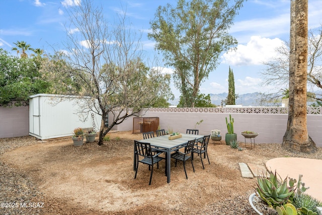 view of patio featuring outdoor dining space, an outbuilding, a fenced backyard, and a shed