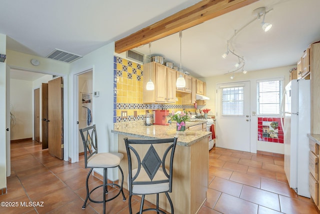 kitchen featuring visible vents, light brown cabinetry, range with gas stovetop, decorative backsplash, and freestanding refrigerator