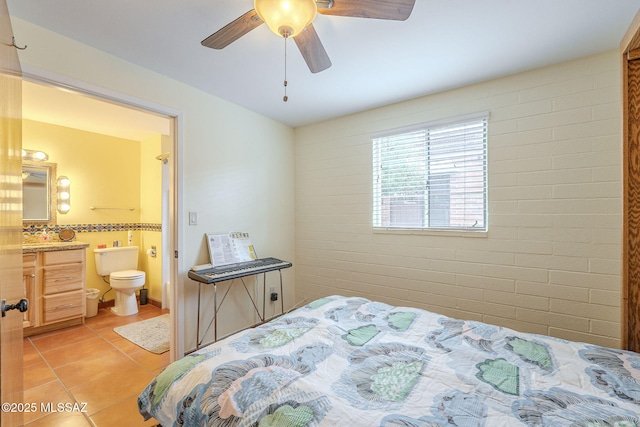 bedroom with light tile patterned floors, connected bathroom, brick wall, and a ceiling fan