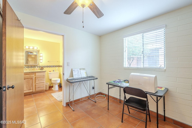 office area with light tile patterned flooring, a ceiling fan, and brick wall