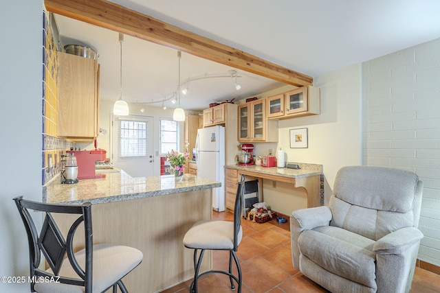 kitchen featuring a peninsula, beam ceiling, freestanding refrigerator, glass insert cabinets, and a kitchen breakfast bar