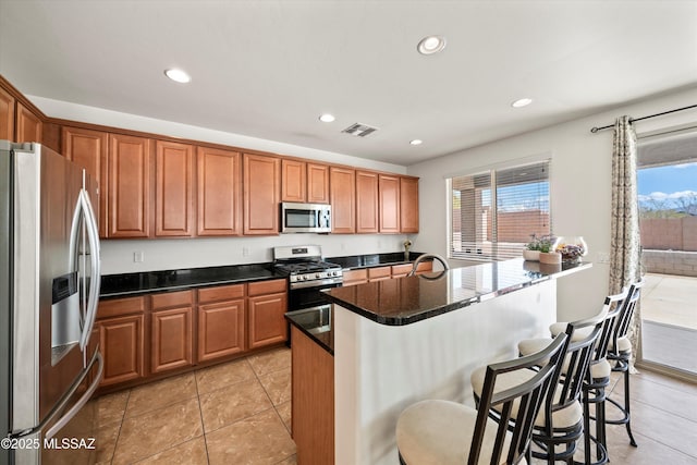 kitchen featuring visible vents, a breakfast bar, brown cabinetry, stainless steel appliances, and a sink