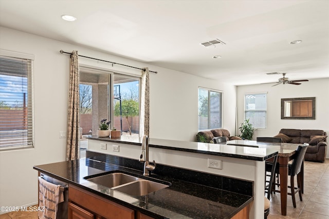 kitchen with visible vents, open floor plan, dark stone counters, brown cabinets, and a sink