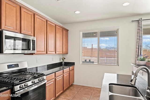 kitchen featuring brown cabinets, a sink, stainless steel appliances, dark stone counters, and light tile patterned floors