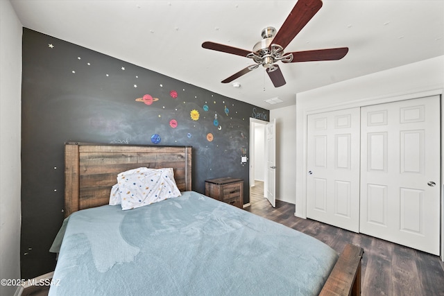 bedroom with wood finished floors, wallpapered walls, ceiling fan, a closet, and an accent wall