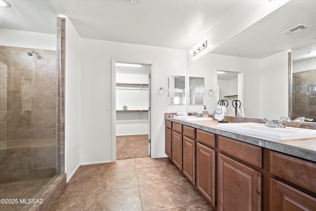 bathroom with visible vents, tiled shower, double vanity, a sink, and a walk in closet