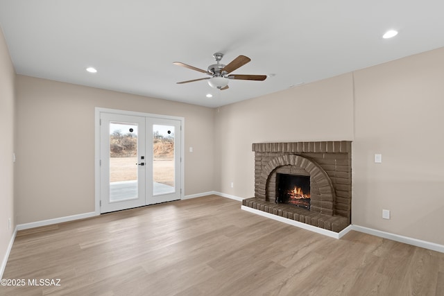 unfurnished living room with a ceiling fan, wood finished floors, recessed lighting, french doors, and a brick fireplace