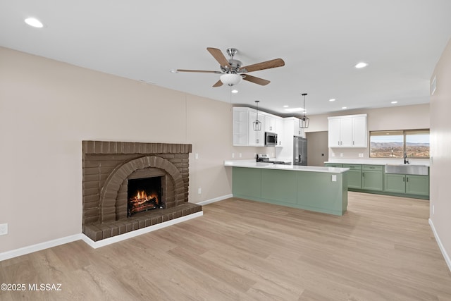 unfurnished living room with a sink, ceiling fan, a fireplace, and light wood finished floors