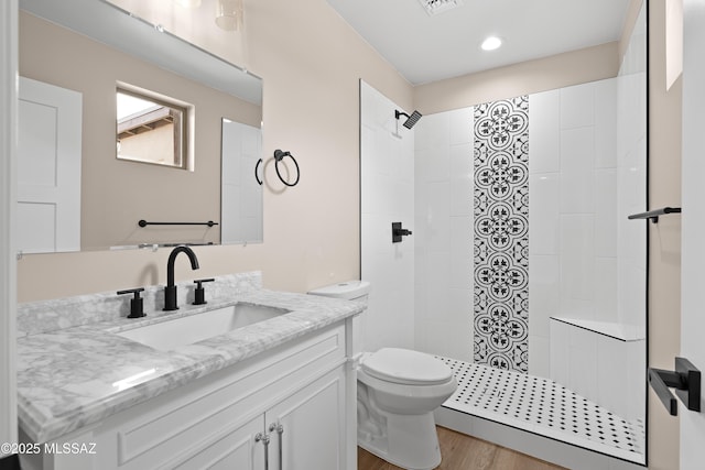 full bathroom with vanity, wood finished floors, visible vents, a tile shower, and toilet