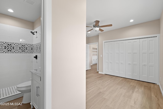 bathroom with wood finished floors, visible vents, tiled shower, ceiling fan, and toilet