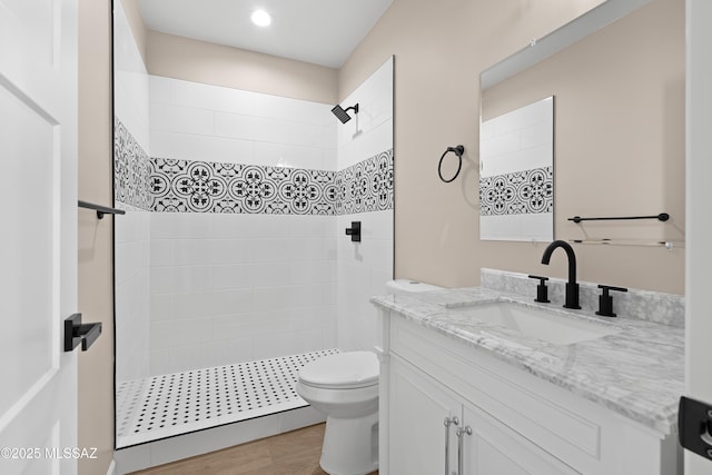 bathroom featuring vanity, toilet, wood finished floors, and tiled shower