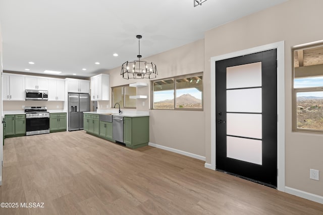 kitchen featuring a sink, stainless steel appliances, light wood-style floors, an inviting chandelier, and green cabinetry