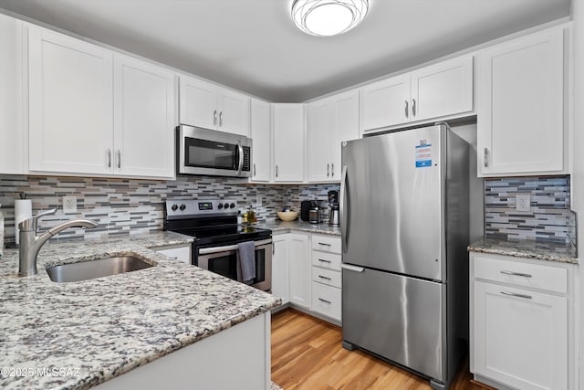 kitchen with light stone countertops, a sink, white cabinets, appliances with stainless steel finishes, and light wood-type flooring