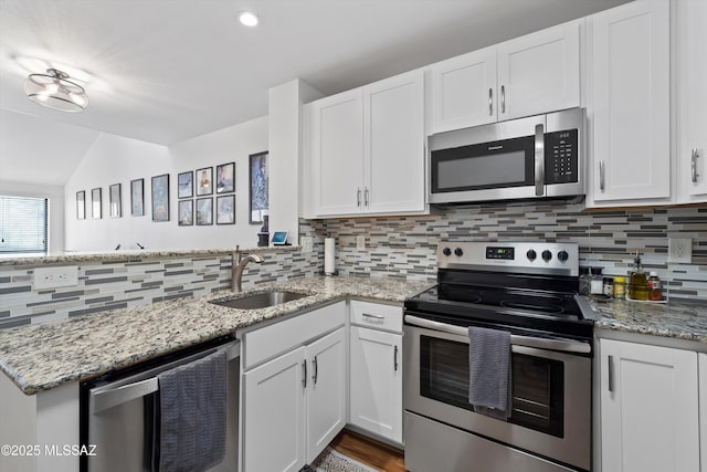 kitchen with decorative backsplash, a peninsula, stainless steel appliances, white cabinetry, and a sink